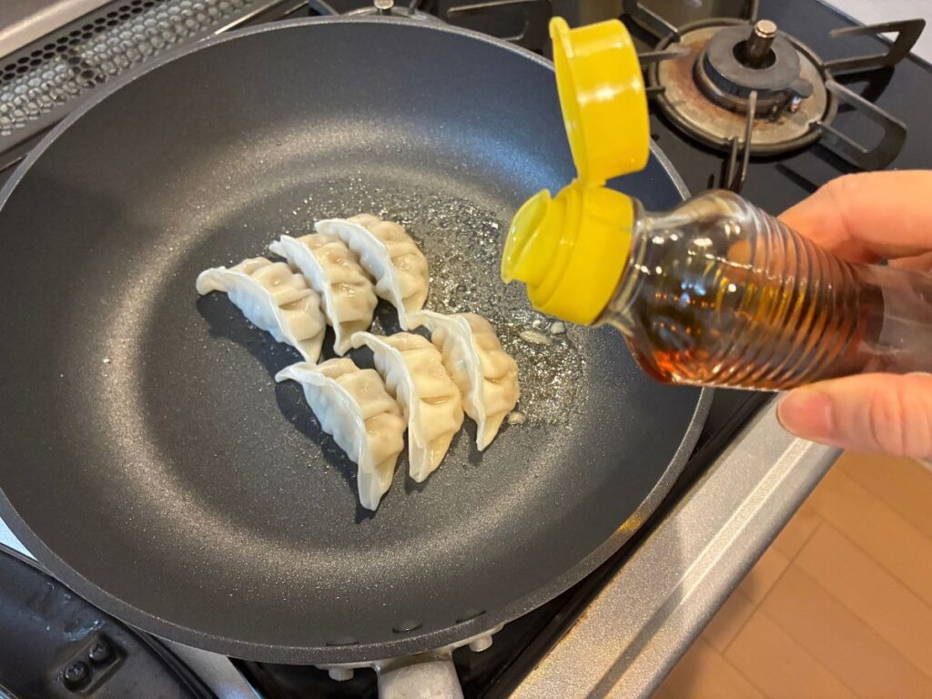 蒸し焼き後の業務スーパー生餃子にごま油を加える様子